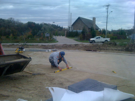 After heights were all figured out, we worked on creating a solid base for the interlock, protecting it from shifting. We allow for small lifts of gravel that get compacted with a plate tamper to reach our 98% compaction which gives you your base. From there we do a final bedding layer which allows us to lay the bricks on a smoother surface. Here he is setting the bars to allow for a consistent slope along the interlock, and also the bedding layer is being pulled by a board (also known as screeding) along the two adjacent pipes.